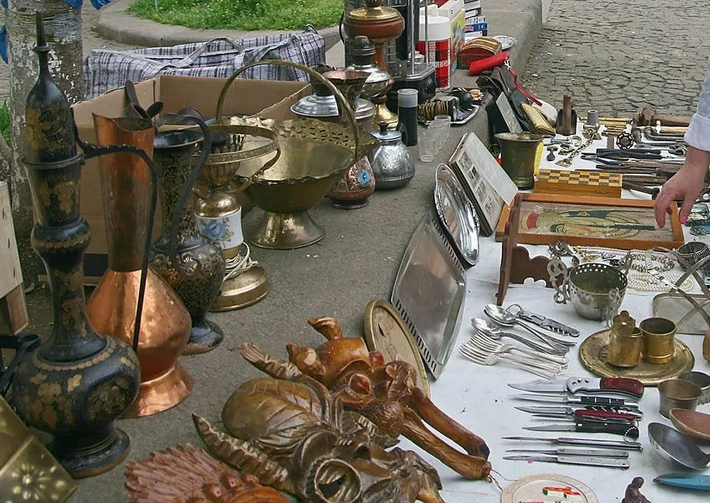 Copper and brass vessels, knives and silverware spread on the pavement at a flea market