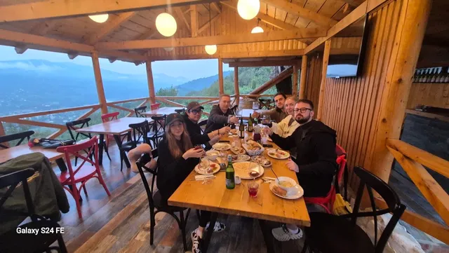 A group of diners around a wooden table on a covered terrace with a wide mountain view