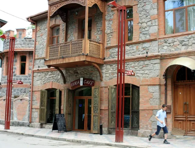 A stone and brick building with wooden balconies, a cafe sign and red pillars along the street