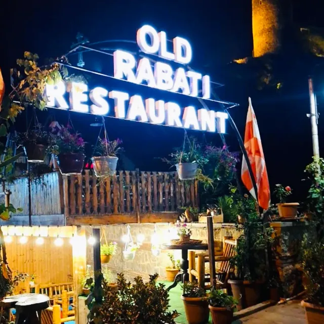 Large illuminated letters above a wooden fence with hanging pots, at night