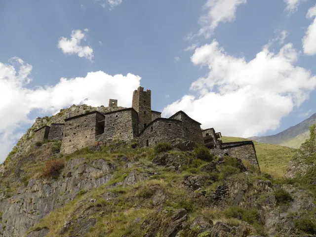 Ruined stone towers on a steep rocky ridge under clouds