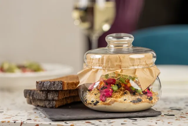 A dish served in a glass jar with slices of toasted bread and a glass of white wine