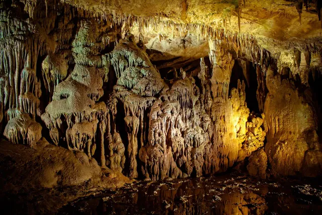 A lit cave hall with stalactites and stalagmites and a visitor walkway below