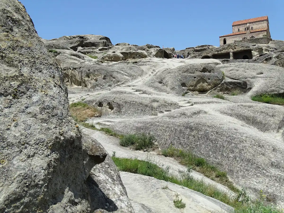 Terraces and caves carved into pale rock rising to a brick church at the top of the hill
