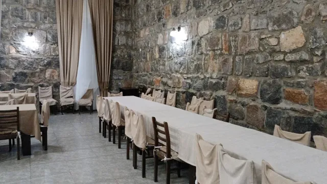 A hall with a rough stone wall, a long table in a light cloth and chairs in fabric covers