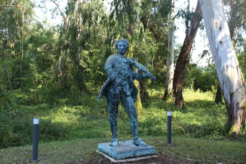 A bronze statue of a musician holding an instrument on a lawn among trees at Musicians Park in Shekvetili