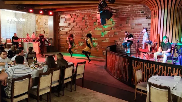Dancers in costume on a performance floor, musicians on a raised stage and diners at tables