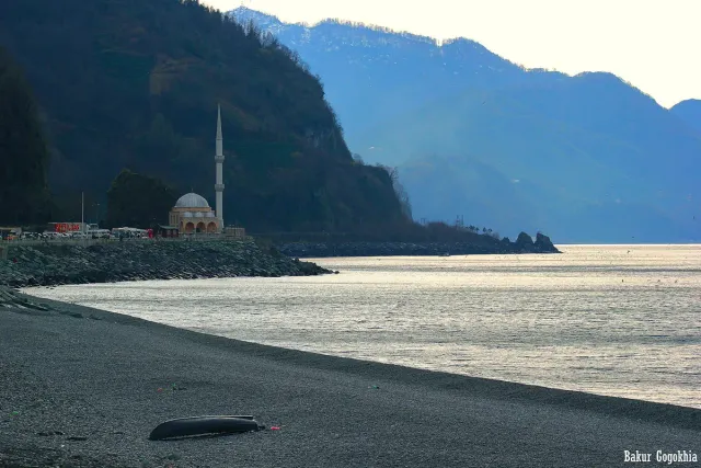 A pebble beach curving towards a mosque and wooded headlands above a silvery sea