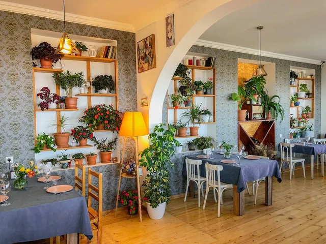 A bright dining room with shelves of potted plants, blue tablecloths and a wooden floor