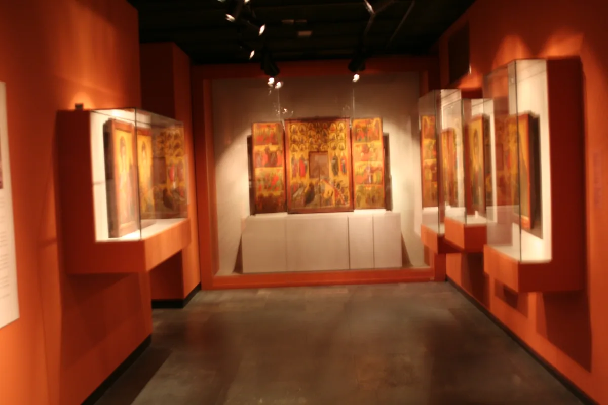 A gallery with orange walls and lit display cases holding gilded icons