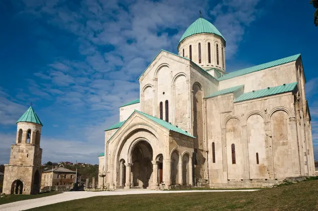 A large stone cathedral with a green dome and arched facade above a lawn