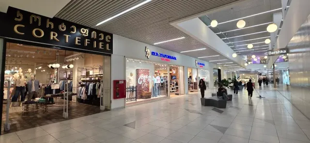 A mall corridor with lit clothing store fronts, benches and shoppers in the walkway
