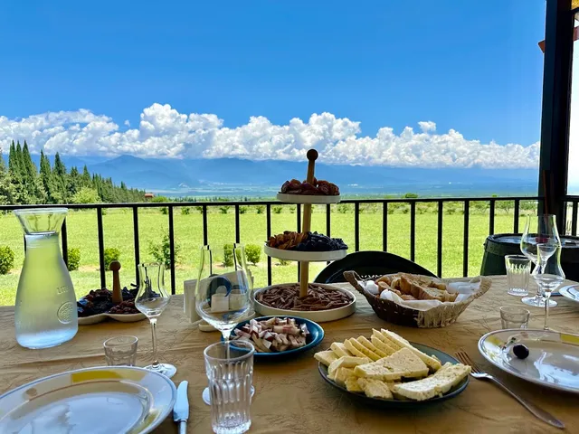 A table set with cheeses, bread and dried fruit facing a vineyard, a valley and mountains