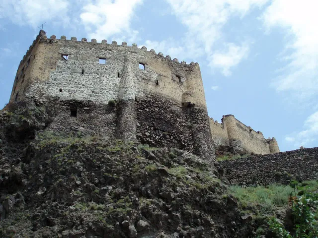 The stone walls and towers of a fortress on a rocky hill