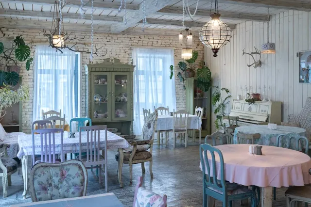 A pastel dining room with cloth covered tables, chandeliers and a green display cabinet