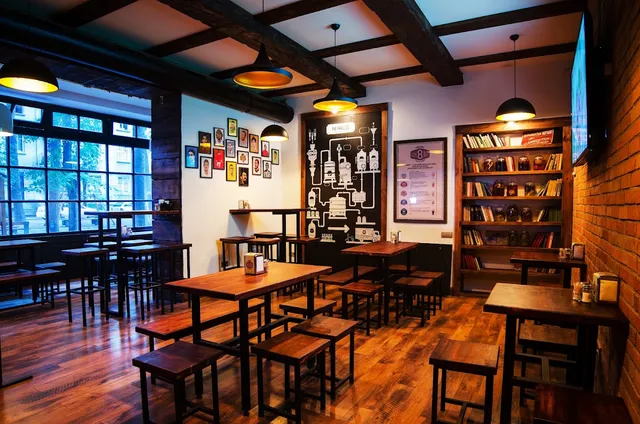 A bar space with high wooden tables, a bottle library and a brewery drawing on the wall