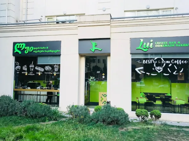 A cafe facade with two large glass fronts, green signage and grass in front
