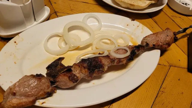 A skewer of grilled meat on a white plate with onion rings, on a light wooden table