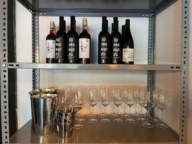 A metal shelf with dark wine bottles, rows of wine glasses and ice buckets