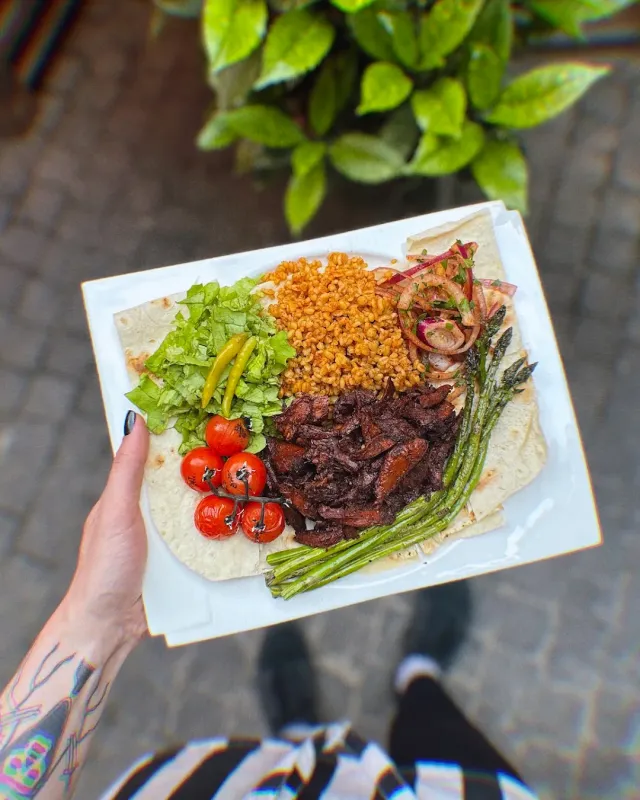 A hand holding a tray with flatbread, grains, lettuce leaves, tomatoes and asparagus