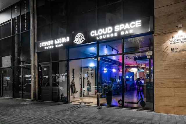 A glass facade lit in the evening with a glowing white sign and a purple-lit interior