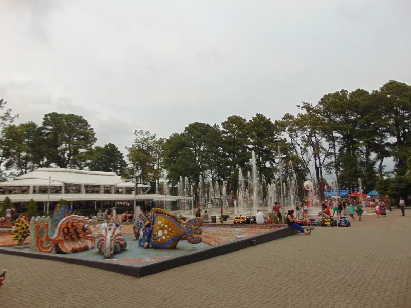 A paved square in Kobuleti Central Park with fountains, colourful sculptures and tall trees around it