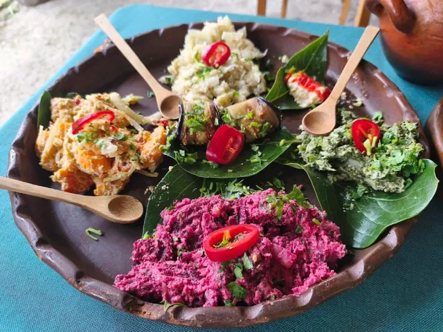 A clay platter with vegetable spreads in purple, green and white, chili and wooden spoons