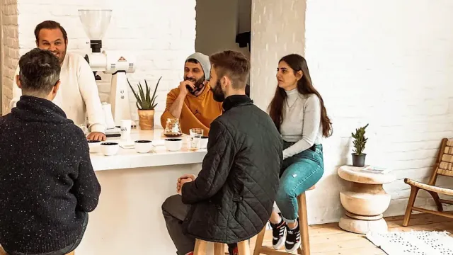 People sitting on stools around a white counter with coffee cups in a bright room
