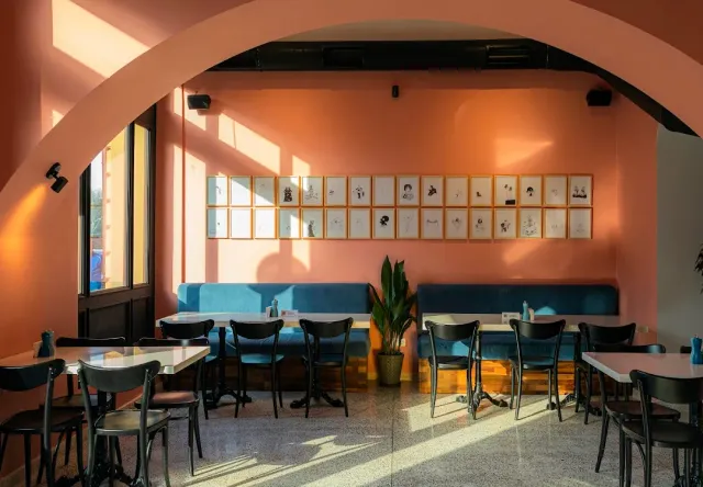 A space with a pink arch, a blue bench, rows of framed drawings and small tables