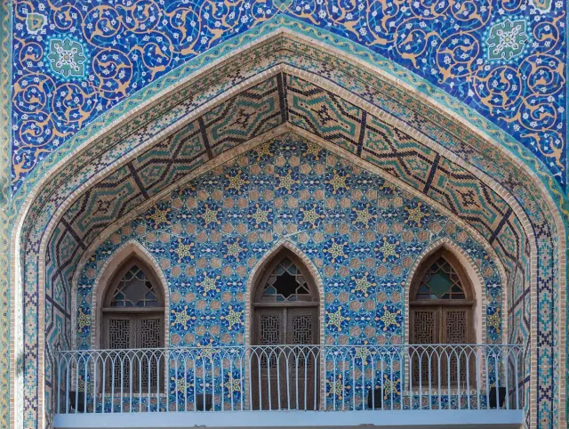 A facade covered in blue mosaic tiles with pointed arches and latticed windows