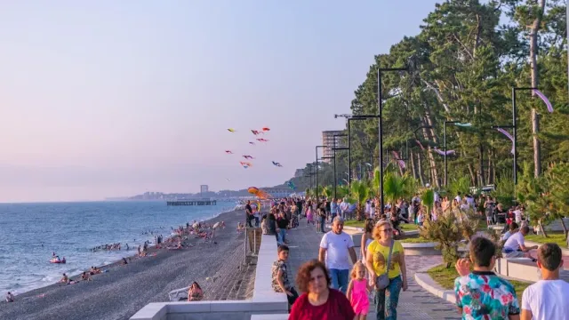 A promenade along a pebble beach in the evening with walkers, pine trees and kites above the sea