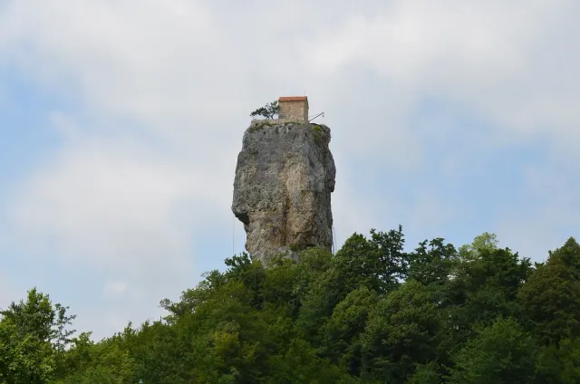 A tall solitary rock pillar topped by a small church and surrounded by forest