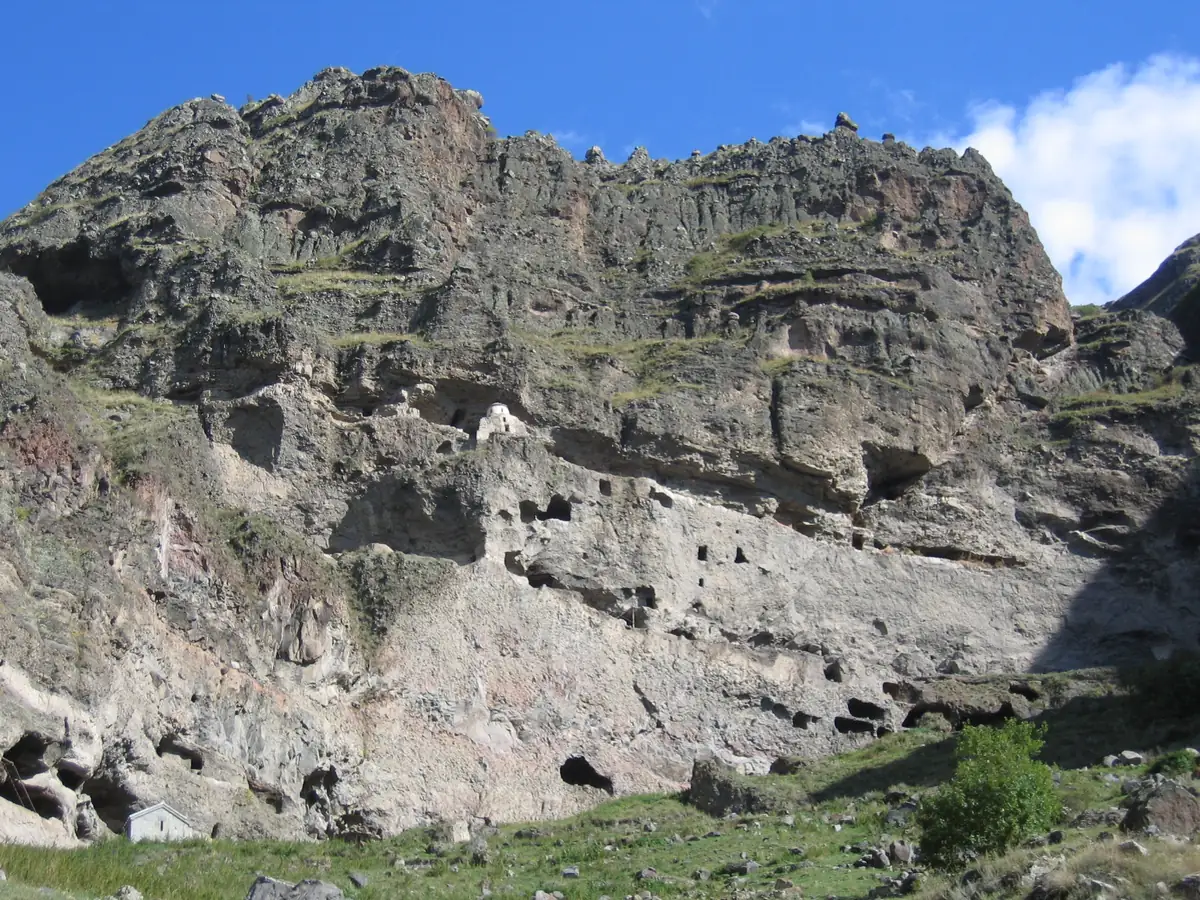 A high rock cliff pierced with rows of carved cave openings under a blue sky