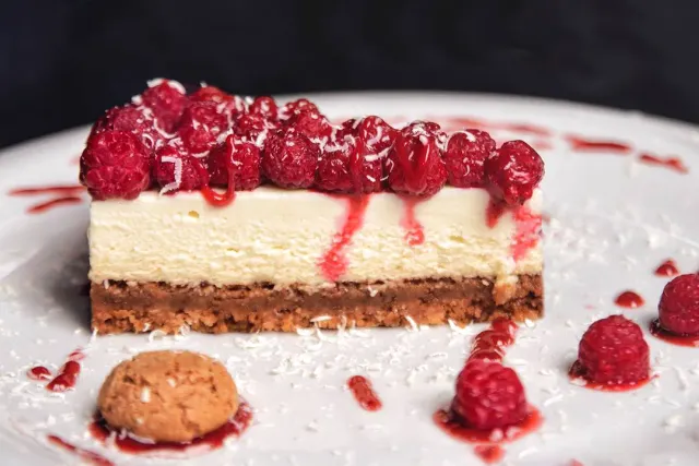 A slice of cheesecake with a layer of raspberries and red sauce on a white plate