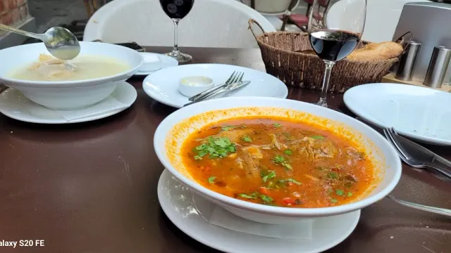 Two bowls of soup, one white and one red with herbs, beside a glass of wine