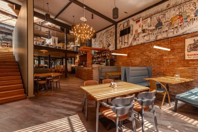 A hall with a brick wall, an illustrated mural, wooden tables and stairs to a mezzanine