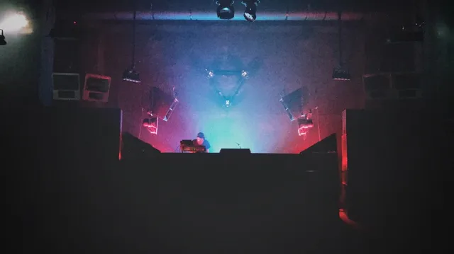 A DJ on a dark stage lit in blue and red lights between speakers