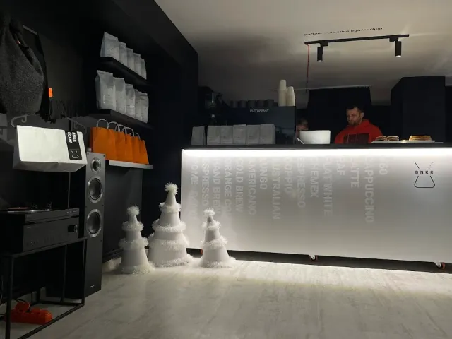 A white-lit coffee counter with a list of drinks, and shelves of bean bags on a dark wall