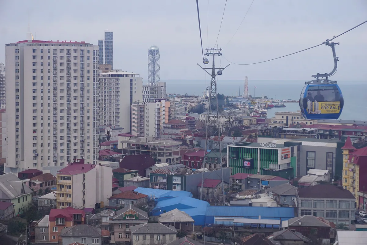 A cable car cabin above city rooftops facing the sea