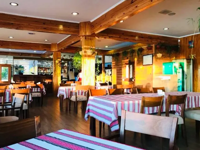 A space with wooden beams and red and white striped cloths, a counter behind and hanging plants