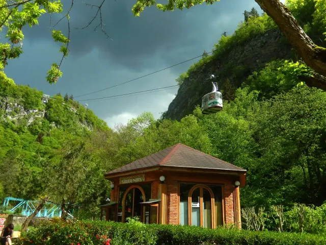 A wooden pavilion in a green park between wooded slopes with a cable car above