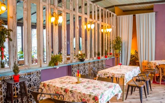 A room with floral tablecloths, a latticed wooden partition, wall lamps and red pots