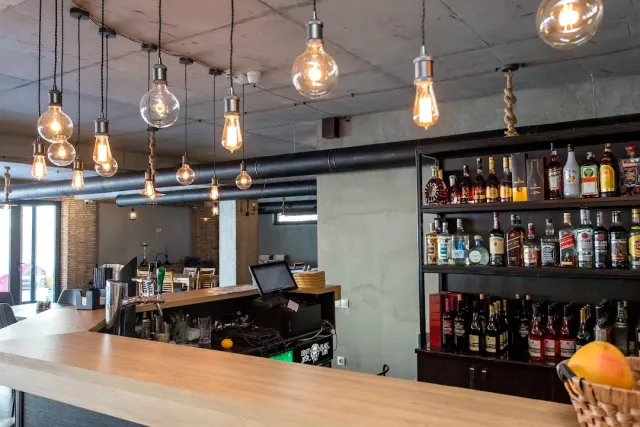 A wooden counter with a row of hanging filament bulbs and a shelf of liquor bottles behind it