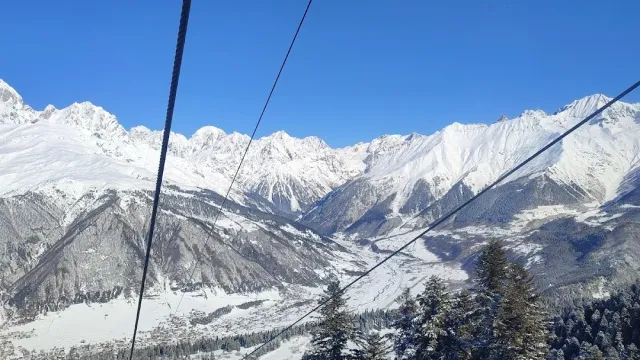 A view from the lift over a snowy ridge and a wide valley, with cables crossing the frame