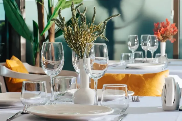 A set table in close view with wine glasses, a vase of dried grasses and yellow cushions