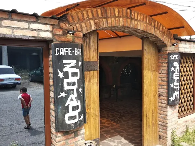 An arched brick entrance with painted black signs, wooden posts and a boy standing outside