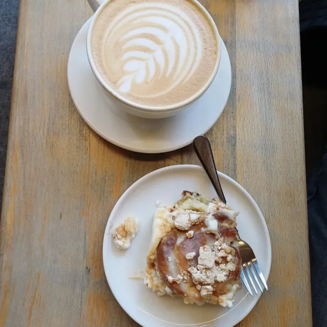 A cappuccino cup with foam art beside a crumb topped pastry on a wooden table