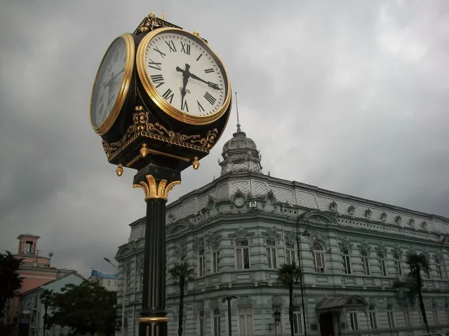 An ornate gilded street clock in front of a grand domed stone building