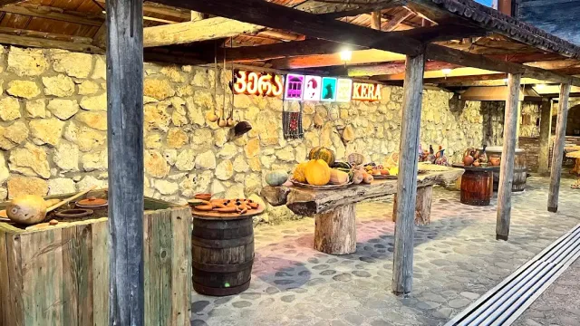 A covered stone veranda with wooden posts, barrels, clay vessels and pumpkins on a table