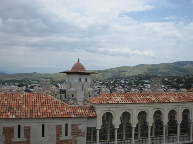 A mosque dome and an arcaded gallery above red tiled roofs with the town and hills beyond